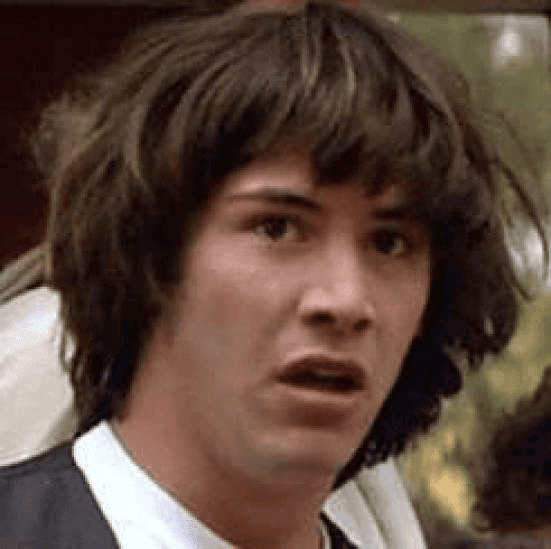 Close-up image of a young Keanu Reeves with shaggy brown hair, a startled wide-eyed expression, and his mouth slightly open while looking toward the camera.