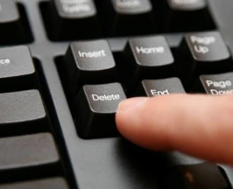 Close-up of a finger pressing the Delete key on a computer keyboard.