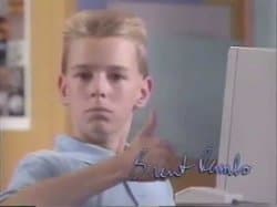 A young boy in a striped shirt sitting at a desktop computer and giving an enthusiastic thumbs-up to the camera