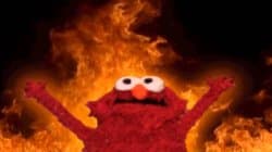 Elmo the Sesame Street muppet standing in a room with flames burning around him, smiling serenely as if nothing is wrong