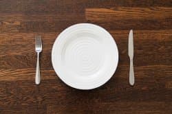 A person sitting at a restaurant table looking down at a completely empty white plate, waiting for food to arrive