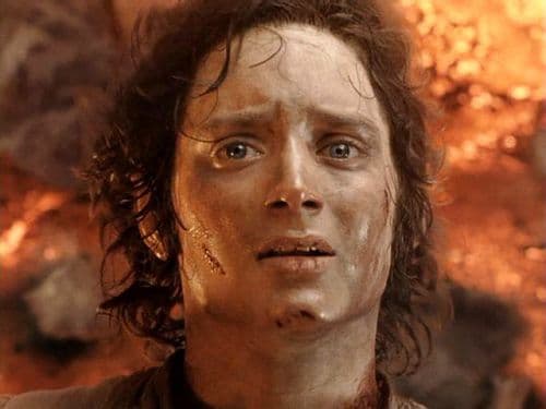Soot-streaked Frodo Baggins looks exhausted and stunned against the orange glow of Mount Doom.