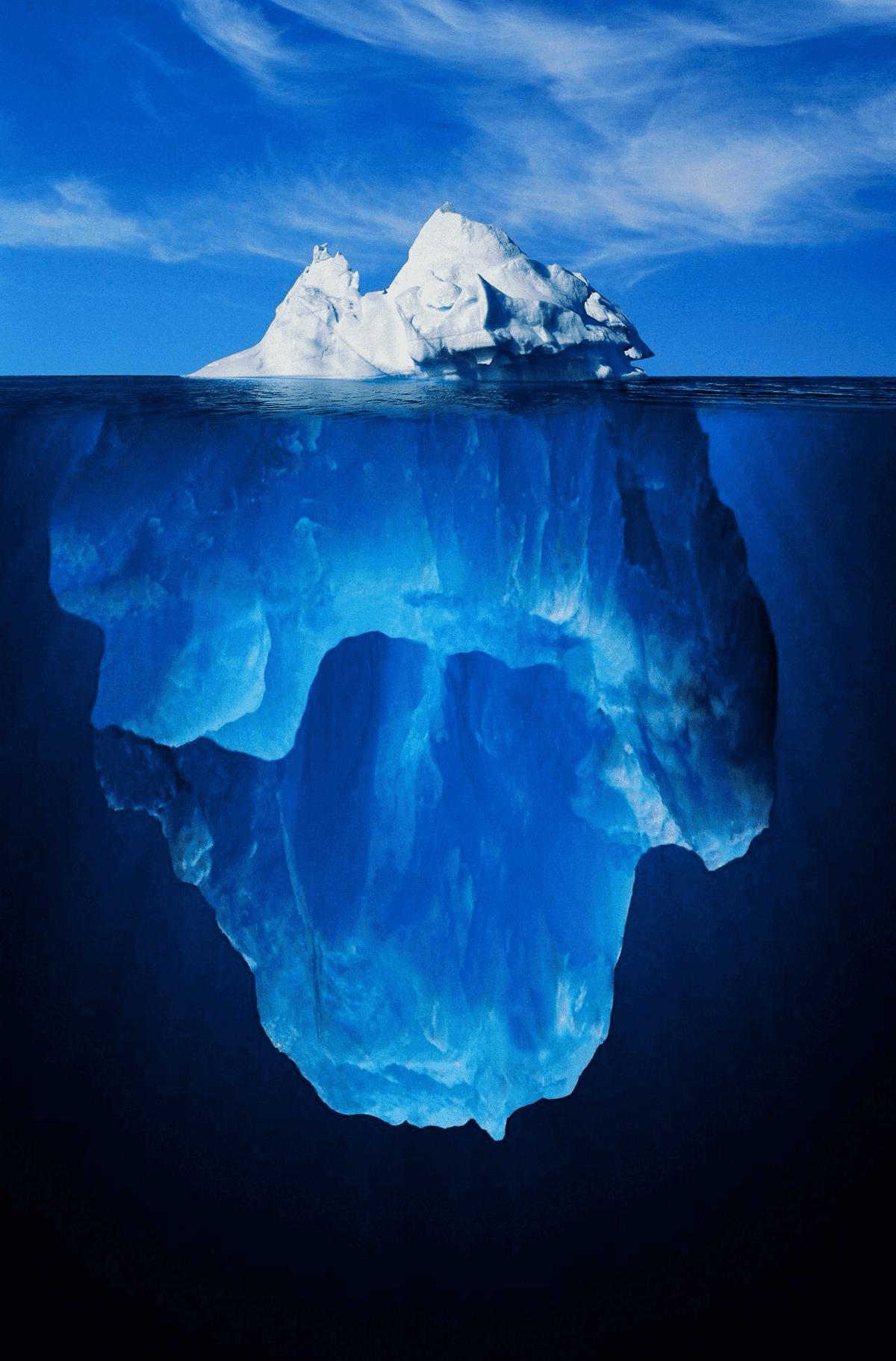 Classic iceberg illustration with a small white tip visible above the waterline against blue sky, and a massive underwater base of ice submerged below in darker blue. Represents the concept that only a small portion is visible to the surface.