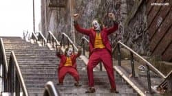 Joaquin Phoenix as the Joker in a red suit dancing with arms spread on a long outdoor stairway in the 2019 Joker film