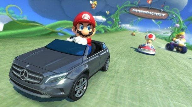 Mario drives a gray Mercedes-Benz on a colorful Mario Kart track, ahead of Toad and Wario in small karts.