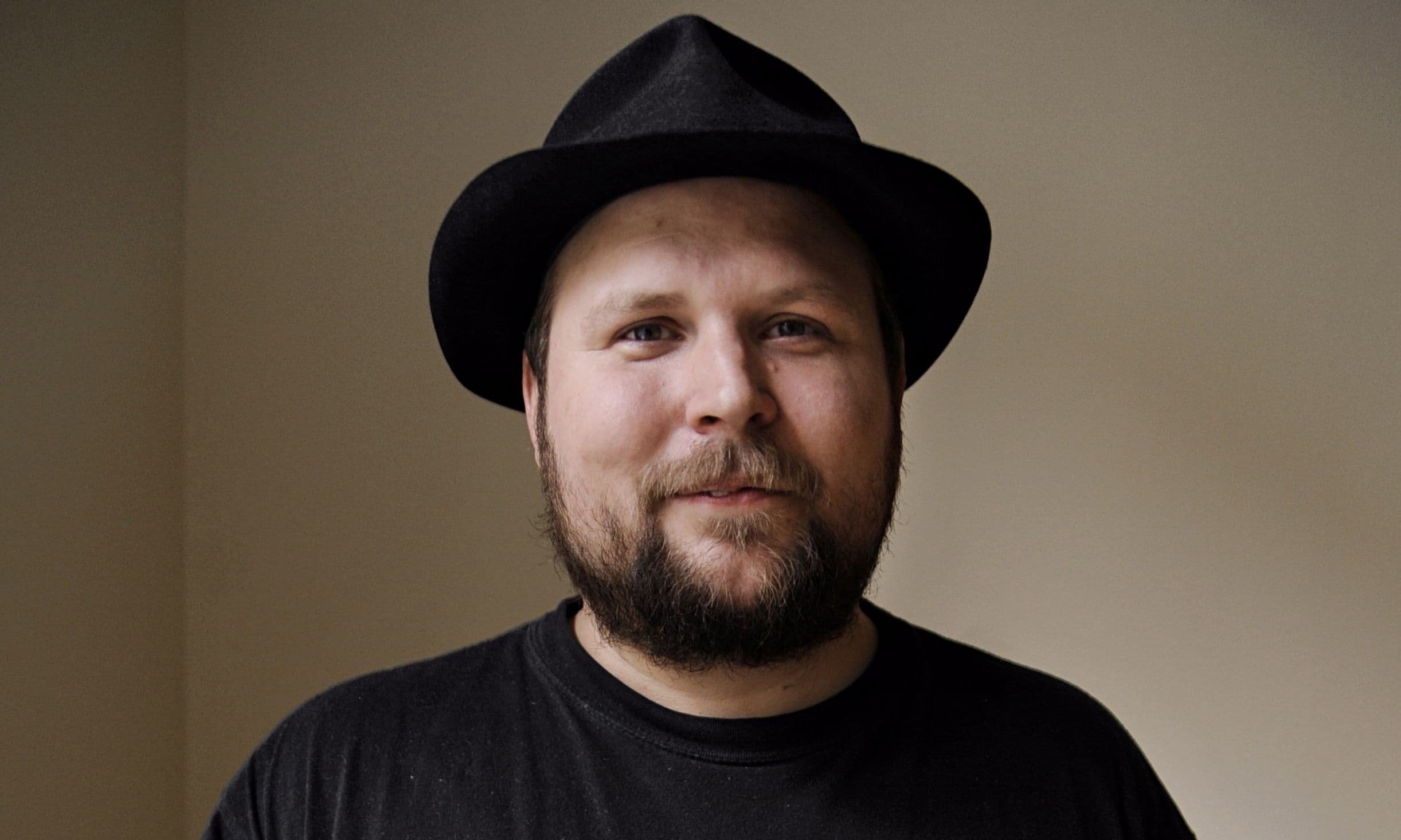 Markus “Notch” Persson wears a black hat and black shirt, smiling slightly at the camera against a plain indoor wall.