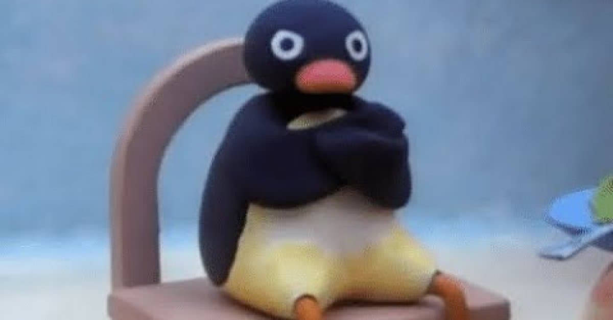 Pingu, a black-and-white clay penguin with an orange beak, sits in a chair with his arms crossed and a wide-eyed, grumpy expression.