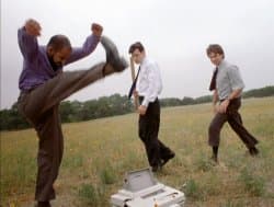 Three men in business casual clothes beating a printer with baseball bats in an open field from Office Space