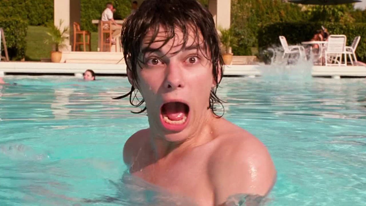 Rodrick Heffley, played by Devon Bostick, stands chest-deep in a swimming pool with wet hair, wide eyes, and his mouth open in a startled scream; a patio and poolside chairs are behind him.