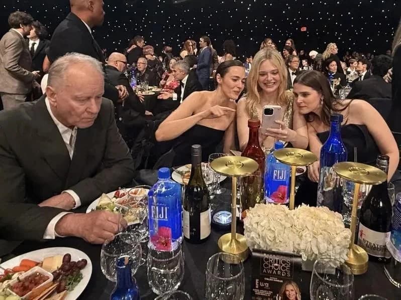 Stellan Skarsgard sits alone while girls take a selfie
