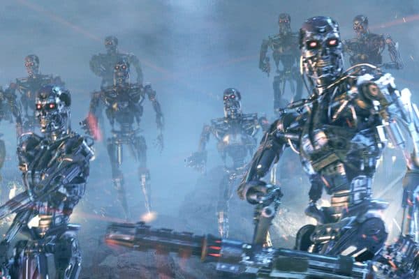 Several silver, red-eyed Terminator endoskeletons advance through a smoky blue battlefield. One large robot fills the right foreground while smaller armed robots approach from the left and background.