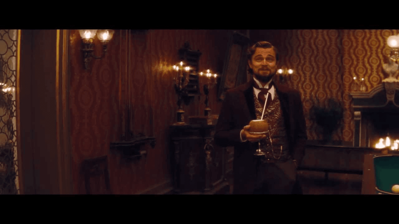 Leonardo DiCaprio as Calvin Candie stands holding a drink in an ornate room, with empty black caption bands above and below the movie still.