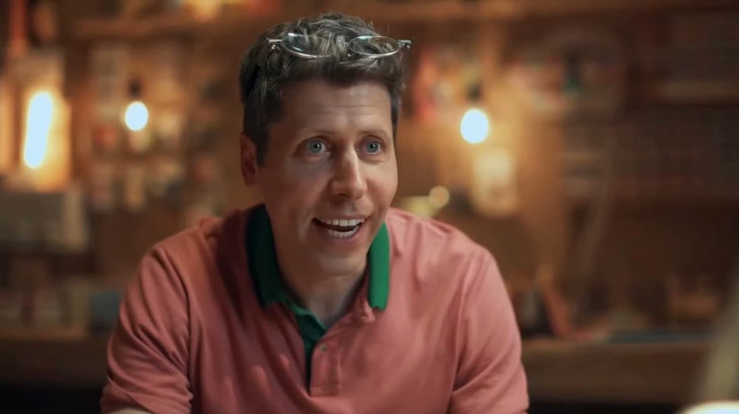 A close-up video still shows a man resembling Sam Altman wearing a salmon-colored polo shirt and glasses on his head, smiling toward the camera in a warmly lit restaurant or lounge.
