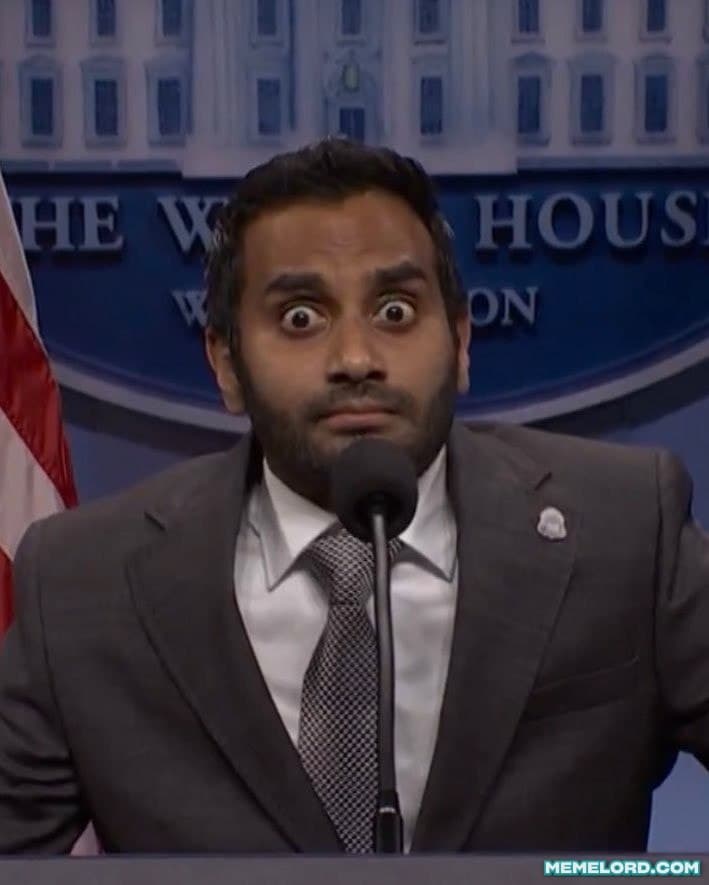 A suited man with wide, startled eyes stands behind a microphone at a White House press briefing podium, with the White House backdrop and part of an American flag visible behind him.
