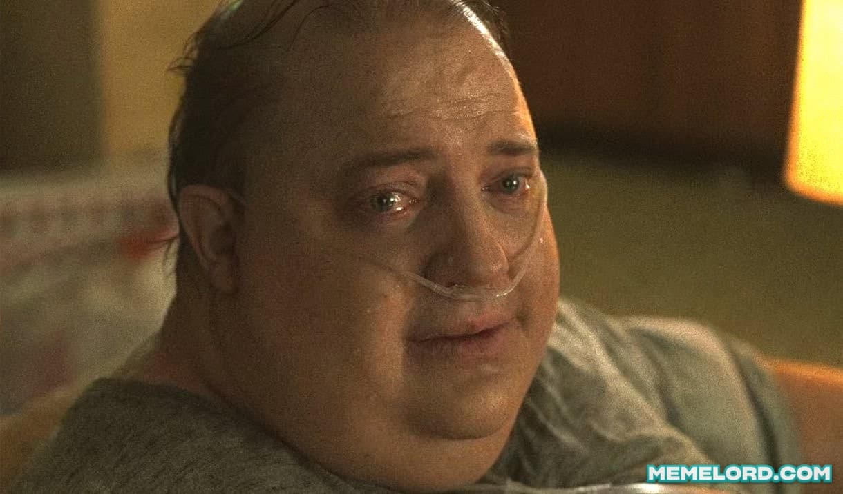 Close-up movie still of Brendan Fraser lying down with watery eyes and a nasal oxygen tube, looking sadly toward the camera in warm, dim lighting.