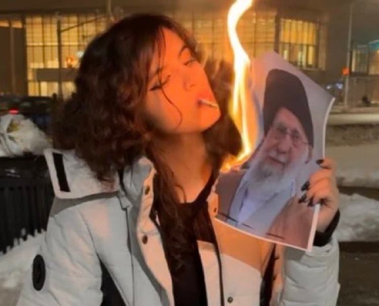 Iranian women lighting a cigarette by burning images of the Ayatollah