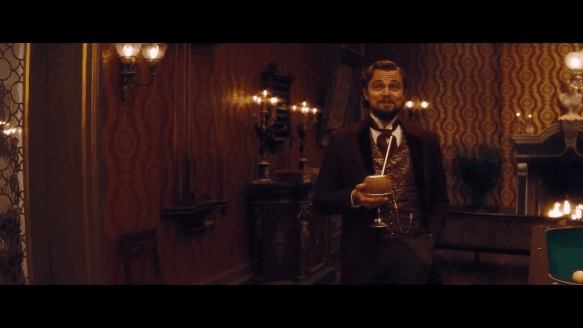 Leonardo DiCaprio as Calvin Candie stands holding a drink in an ornate room, with empty black caption bands above and below the movie still.